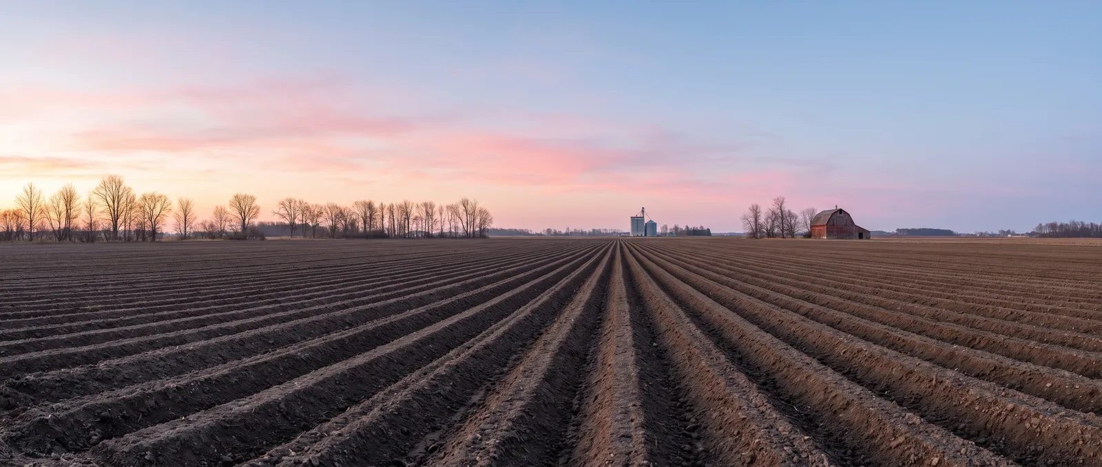 Ploughed field at sunrise with a silo and red barn